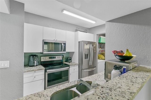 kitchen featuring light stone counters, white cabinets, appliances with stainless steel finishes, and sink