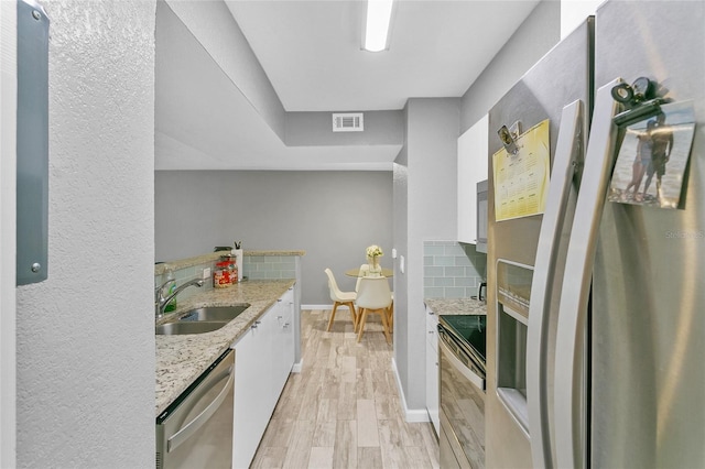 kitchen with white cabinetry, stainless steel appliances, backsplash, light stone countertops, and sink