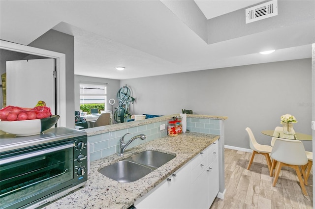 kitchen with light stone countertops, white cabinets, sink, backsplash, and light wood-type flooring