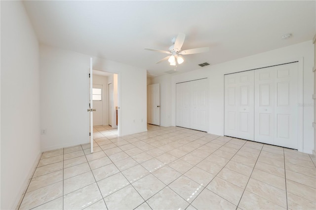 unfurnished bedroom with ceiling fan, light tile patterned floors, and two closets