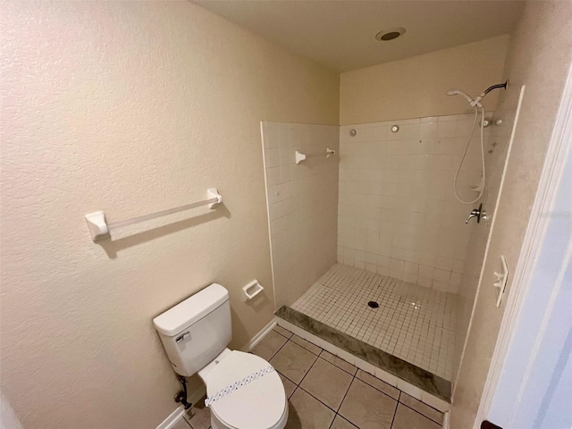 bathroom with toilet, tile patterned flooring, and tiled shower