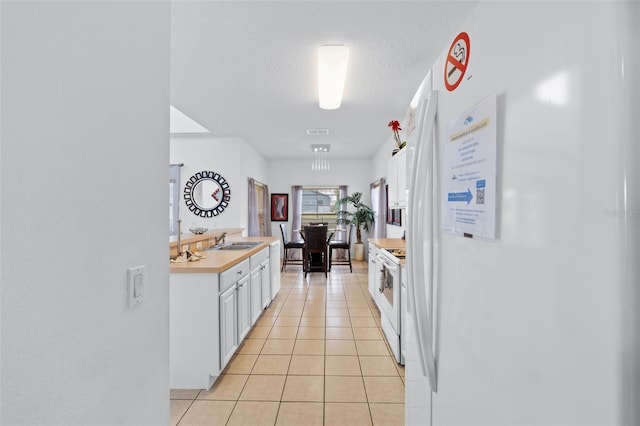 kitchen with white appliances, sink, light tile patterned floors, a textured ceiling, and white cabinetry