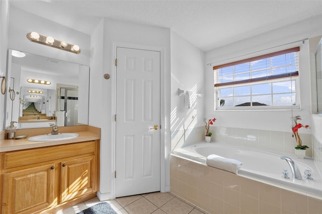 bathroom with tile patterned flooring, a textured ceiling, vanity, and tiled bath