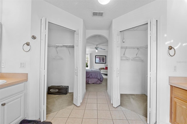 256 Lancaster Dr, Davenport, FL 33897 - ensuite bathroom featuring vanity, a walk in closet, ceiling fan, tile patterned floors, and a textured ceiling