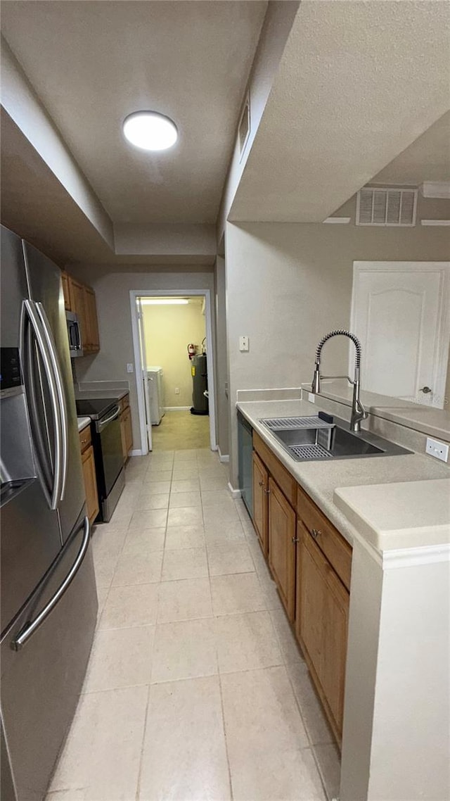 kitchen with a textured ceiling, stainless steel appliances, washer / clothes dryer, light tile patterned flooring, and sink