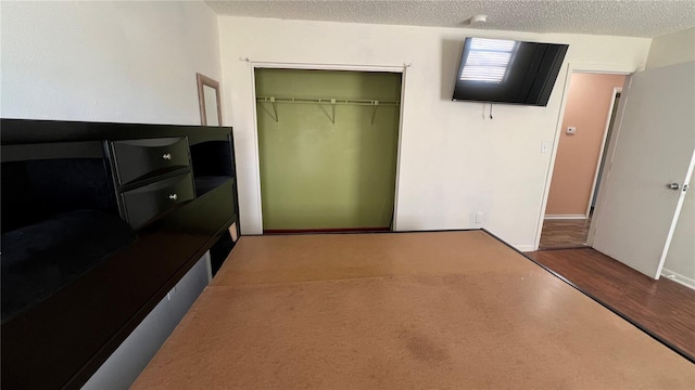 unfurnished bedroom featuring baseboards, a closet, a textured ceiling, and wood finished floors