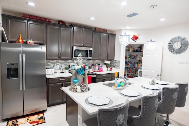 kitchen with appliances with stainless steel finishes, sink, pendant lighting, a center island with sink, and light tile patterned flooring