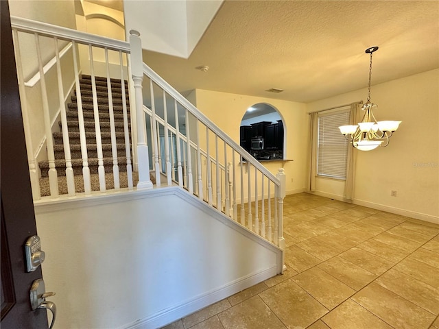 stairway featuring a textured ceiling and a chandelier