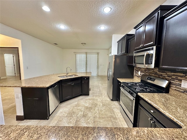 kitchen with a textured ceiling, a kitchen island with sink, decorative backsplash, sink, and stainless steel appliances