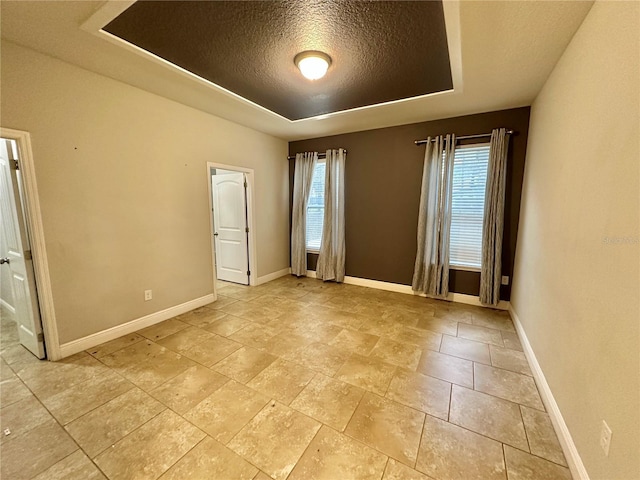 spare room featuring a textured ceiling, light tile patterned floors, and a tray ceiling