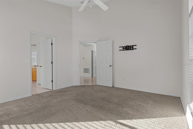 empty room with ceiling fan, light colored carpet, and a high ceiling