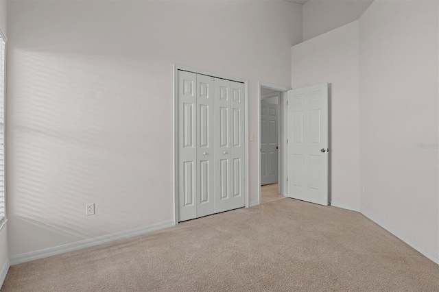 unfurnished bedroom with light colored carpet, a high ceiling, and a closet