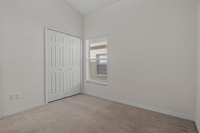 unfurnished bedroom featuring light colored carpet, a closet, and lofted ceiling