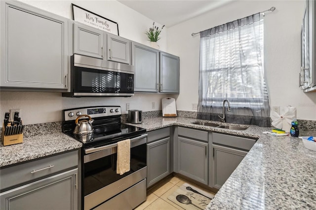 kitchen featuring light stone countertops, stainless steel appliances, sink, light tile patterned floors, and gray cabinets