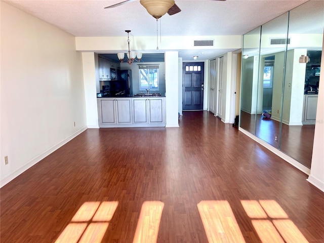 unfurnished living room with dark hardwood / wood-style flooring, sink, ceiling fan with notable chandelier, and a textured ceiling