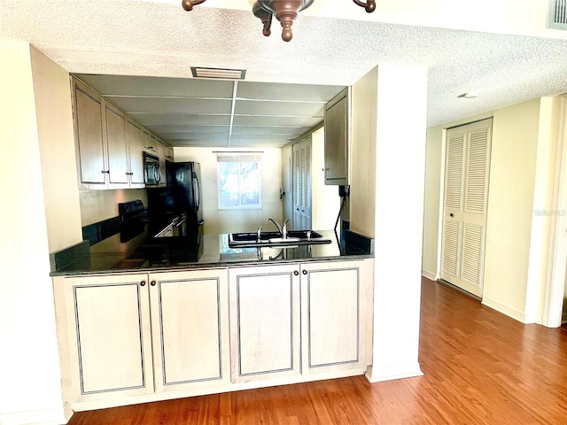 kitchen with a textured ceiling, light hardwood / wood-style floors, black appliances, and sink