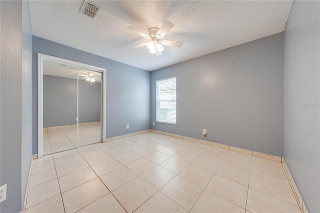 spare room with a textured ceiling, light tile patterned flooring, and ceiling fan