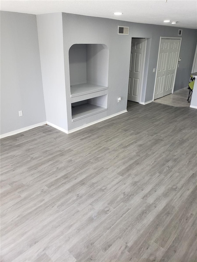 unfurnished living room with built in shelves and hardwood / wood-style floors