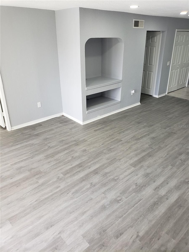 unfurnished living room featuring built in shelves and wood-type flooring