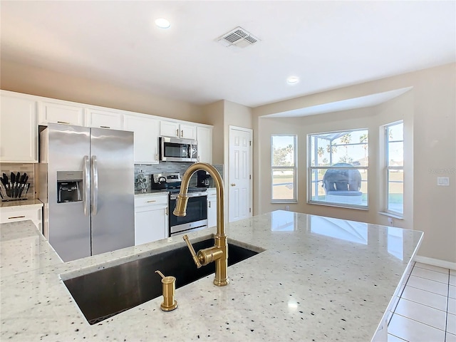 kitchen featuring tasteful backsplash, light stone counters, stainless steel appliances, sink, and white cabinets