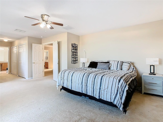 carpeted bedroom featuring multiple closets, ensuite bathroom, and ceiling fan