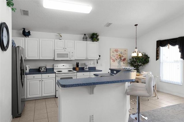 kitchen with a breakfast bar, white appliances, white cabinets, light tile patterned floors, and a textured ceiling