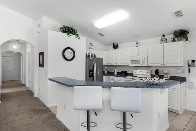 kitchen with a breakfast bar, white cabinetry, white appliances, and vaulted ceiling