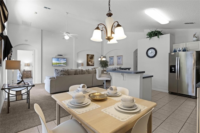 dining space with a textured ceiling, ceiling fan with notable chandelier, light carpet, and vaulted ceiling