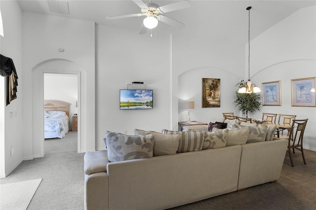 carpeted living room with ceiling fan with notable chandelier and high vaulted ceiling