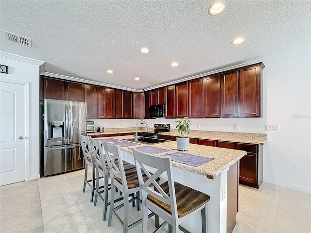 kitchen featuring stainless steel fridge, a kitchen breakfast bar, electric range oven, sink, and an island with sink