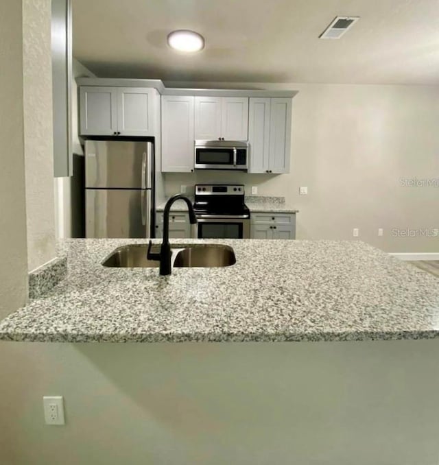 kitchen featuring light stone countertops, white cabinetry, sink, stainless steel appliances, and kitchen peninsula