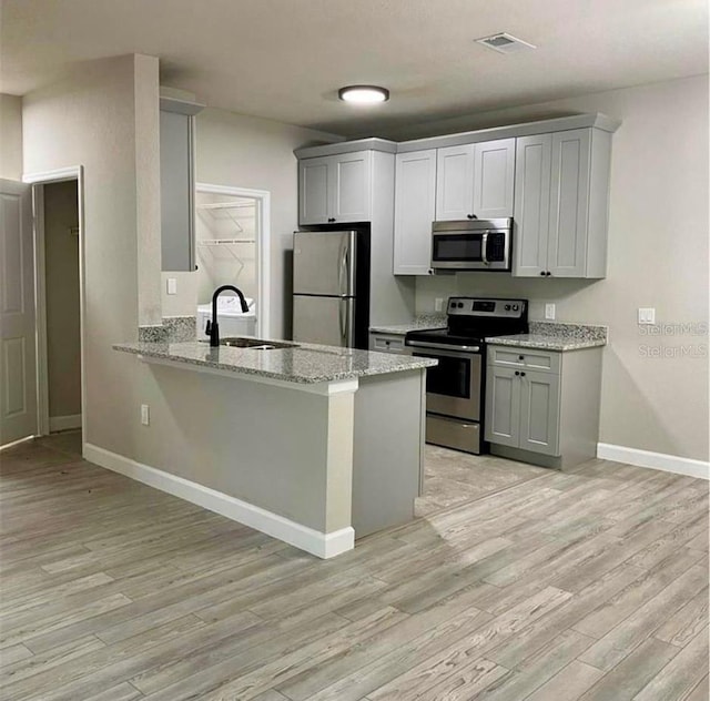 kitchen with kitchen peninsula, light wood-type flooring, light stone counters, stainless steel appliances, and sink