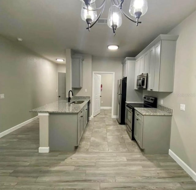 kitchen with gray cabinetry, sink, light stone counters, a chandelier, and appliances with stainless steel finishes