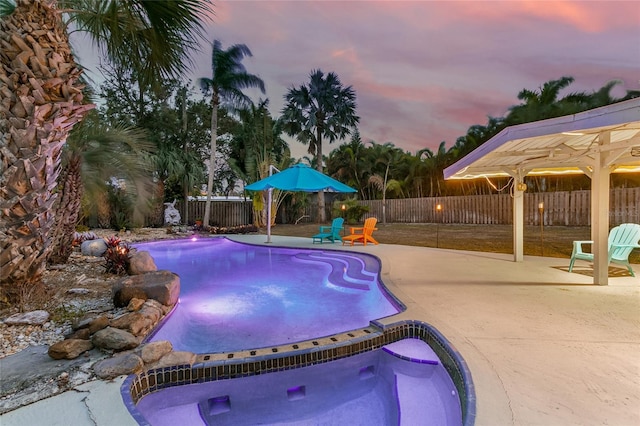 pool at dusk with an in ground hot tub and a patio area