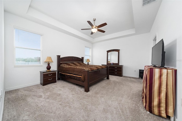 carpeted bedroom with ceiling fan and a tray ceiling