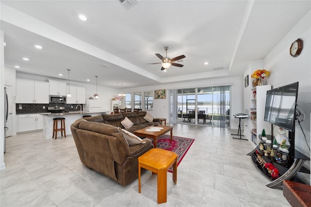 living room with ceiling fan with notable chandelier, sink, and a tray ceiling