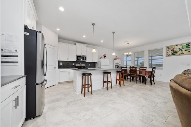 kitchen with a breakfast bar area, an island with sink, decorative light fixtures, white cabinetry, and stainless steel appliances