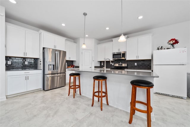 kitchen featuring an island with sink, pendant lighting, a breakfast bar area, white cabinets, and appliances with stainless steel finishes