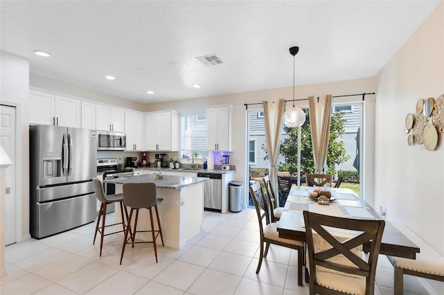 kitchen with light stone counters, stainless steel appliances, a kitchen island, decorative light fixtures, and white cabinetry