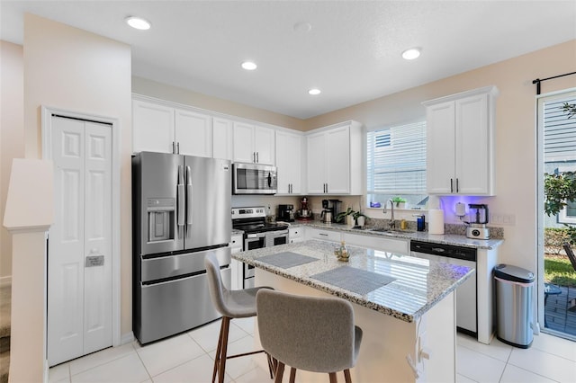 kitchen featuring light stone countertops, stainless steel appliances, sink, white cabinets, and a center island