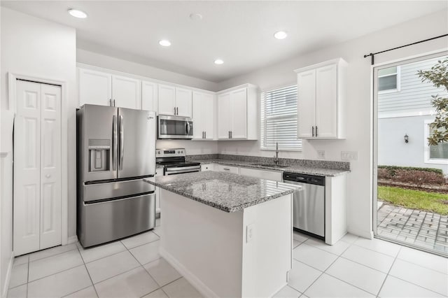 kitchen with light stone counters, light tile patterned flooring, stainless steel appliances, a sink, and white cabinets