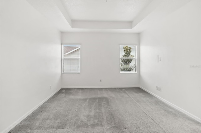 carpeted empty room featuring a tray ceiling and baseboards