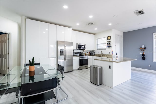 kitchen with white cabinetry, sink, light stone counters, appliances with stainless steel finishes, and light wood-type flooring