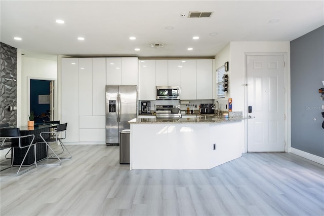 kitchen featuring light stone countertops, stainless steel appliances, kitchen peninsula, light hardwood / wood-style floors, and white cabinets