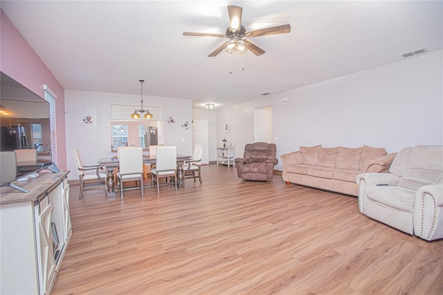 living room with ceiling fan with notable chandelier, a textured ceiling, and light hardwood / wood-style flooring