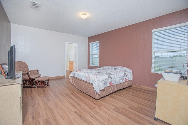 bedroom featuring a textured ceiling, ensuite bath, multiple windows, and light wood-type flooring