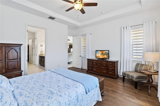 bedroom with a raised ceiling, connected bathroom, ceiling fan, and hardwood / wood-style flooring