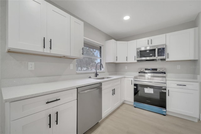 kitchen with sink, white cabinets, appliances with stainless steel finishes, and light wood-type flooring