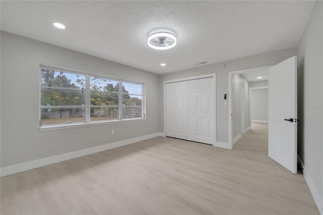 unfurnished bedroom with a textured ceiling, a closet, and light wood-type flooring