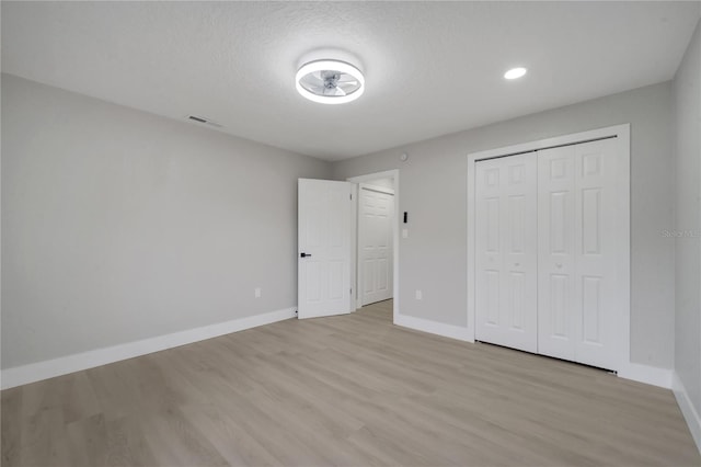 unfurnished bedroom with a textured ceiling, a closet, and light wood-type flooring